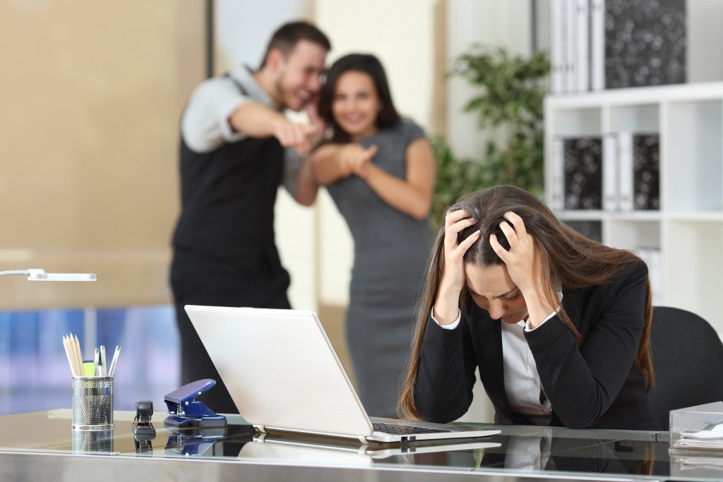 Two businesspeople bullying a sad colleague that is sitting in her workplace at office